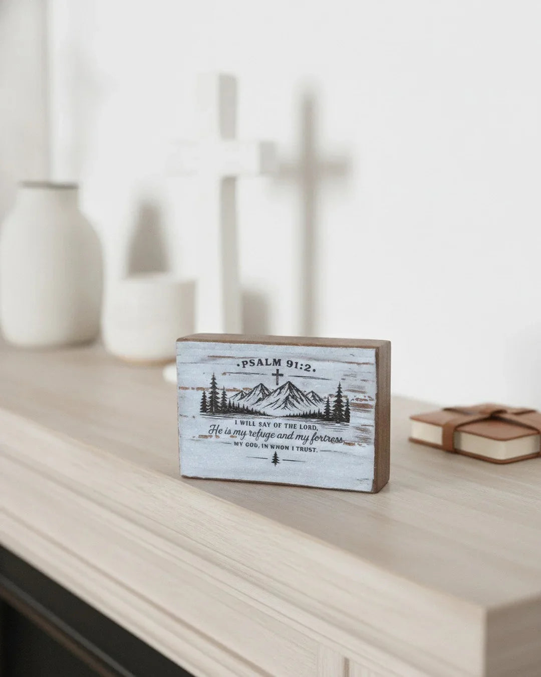 Wooden home decor with Psalm 91:2 scripture, mountain design, and cross, displayed on a shelf.